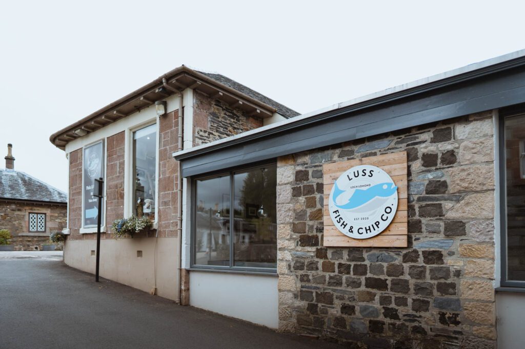The shop's front with its round sign, in Luss.