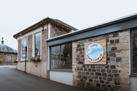 The shop's front with its round sign, in Luss.