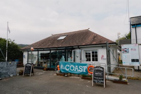 White cottage-style building with a "Coast" banner and chalkboard signs outside