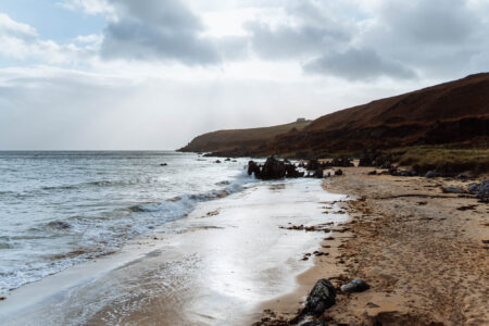 The Singing Sands, a curve of pale sand below a brown headland, waves washing in.