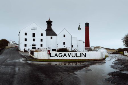 The white front of Lagavulin with its name on the wall and the red chimney behind.