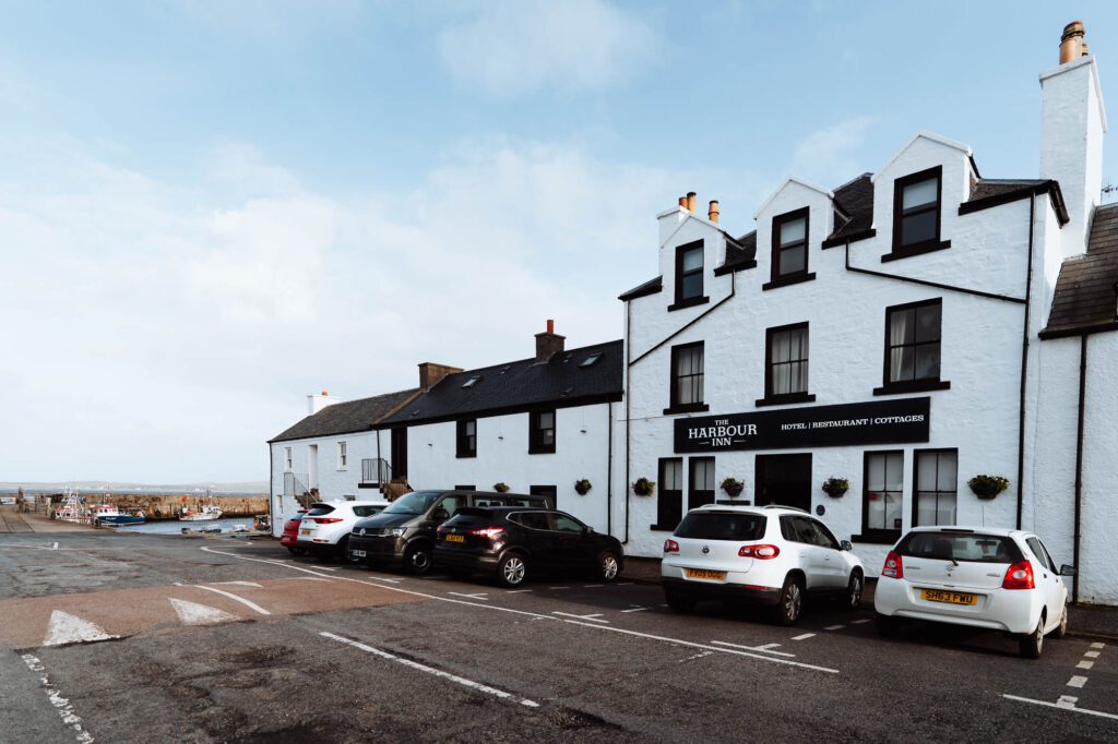 The whitewashed Harbour Inn in Bowmore under a blue sky, cars parked in front.