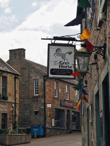 The Grey Horse pub sign hangs above a quiet Scottish street with bunting
