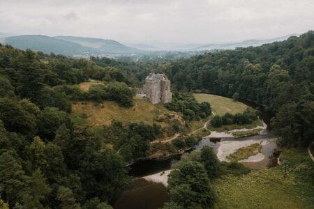 Turreted castle above a winding river, surrounded by dense woodland and hills