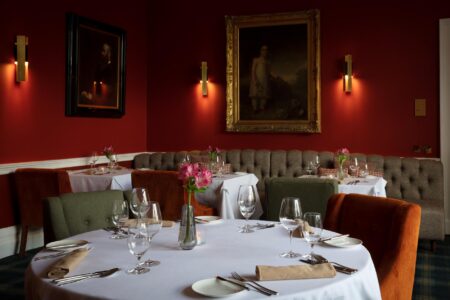 Red dining room with gilt-framed portraits, wall lights and set tables