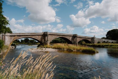 Stone arched bridge spanning a wide river beneath a cloudy blue sky