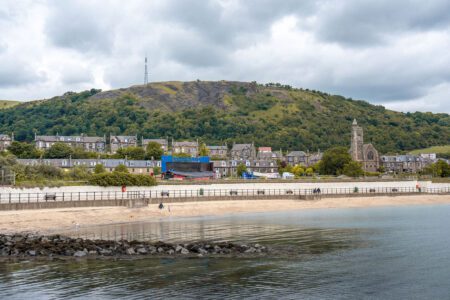 Sandy beach and promenade beneath Gourock's hillside, church spire rising above the seafront