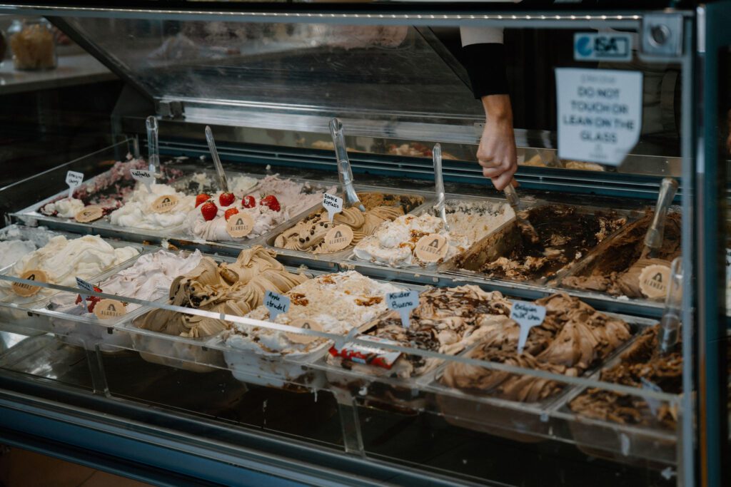 Gelato display case with a "do not touch or lean on glass" sign