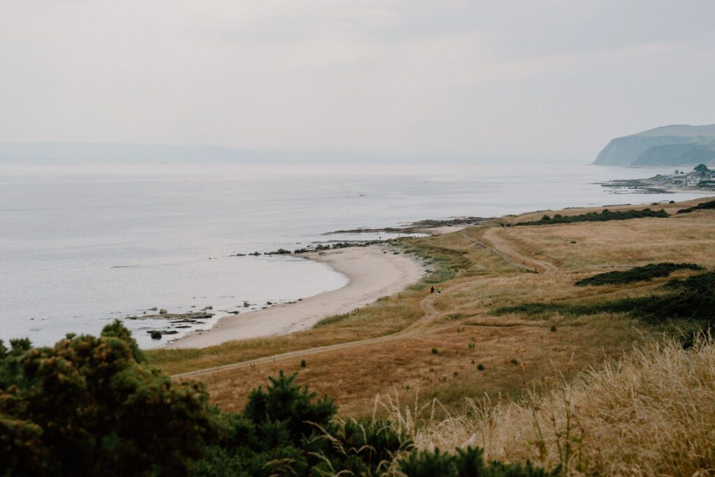 Grassy coastal path curving above a rocky shoreline under grey skies