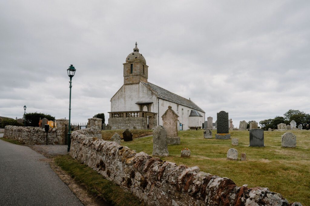 Whitewashed church with bell tower behind a graveyard and stone wall
