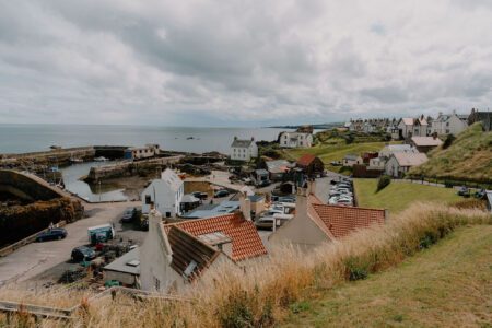 Coastal village with harbour, rooftops and parked cars beside grassy cliffs