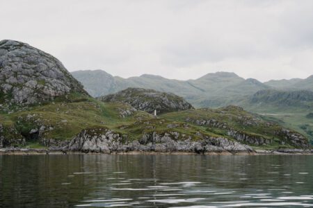Rocky, moss-covered hills rise above a calm loch with distant mountains