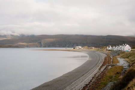 Curved shingle beach beside white cottages, hills rising under cloudy skies