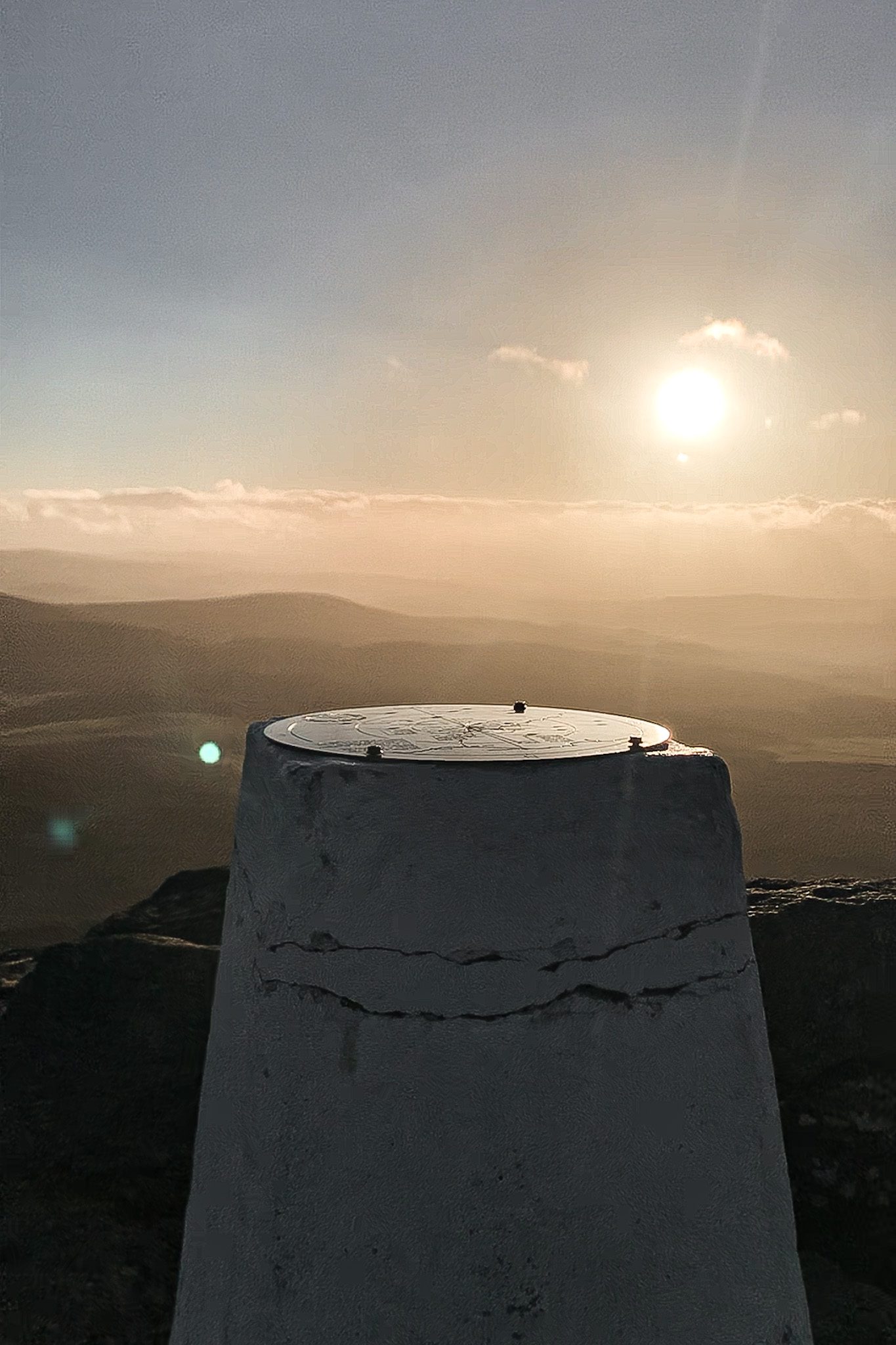 Concrete trig point overlooking layered hills at sunset