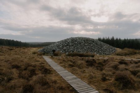 Wooden boardwalk leads to a stone cairn amid moorland and forest