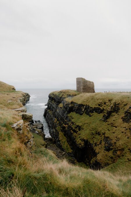 Ruined tower on grassy clifftop above a narrow sea inlet