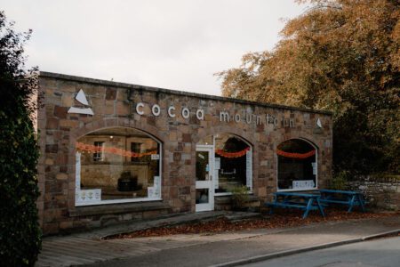 Stone building with arched windows bearing the sign Cocoa Mountain, blue picnic bench outside