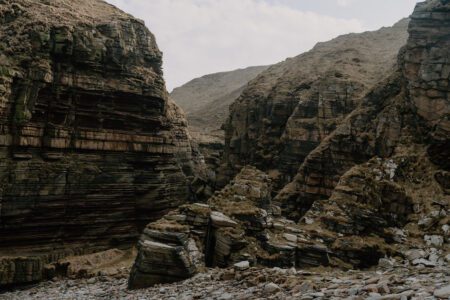 Layered rock cliffs rising above a narrow, boulder-strewn coastal gorge