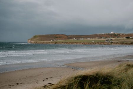 Waves roll onto a sandy beach beneath a headland dotted with houses