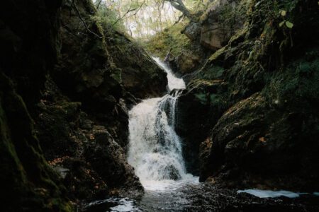 Waterfall cascading through a moss-covered rocky gorge into a dark pool