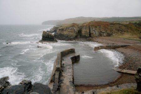 Curved stone harbour walls enclose a pebble beach beneath grey cliffs