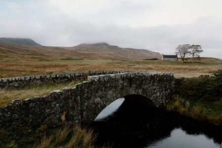 Stone bridge over a dark stream with moorland hills behind