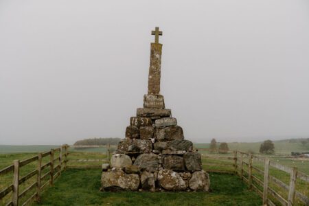 Stone cairn topped with a cross, dated 1857, encircled by fencing