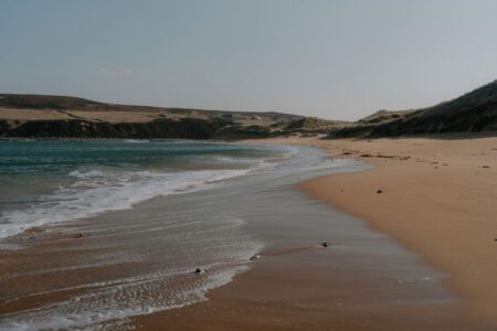 Waves curling onto a curved sandy beach beneath low grassy hills