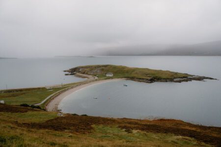 Grassy tidal island linked by a narrow causeway under grey mist