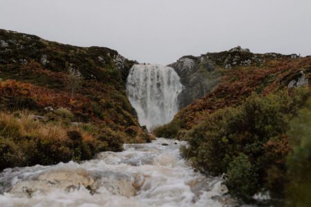 Waterfall cascading between rocky slopes into a fast-flowing stream