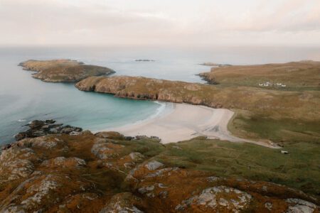 Aerial view of a curved sandy beach between grassy headlands on the coast
