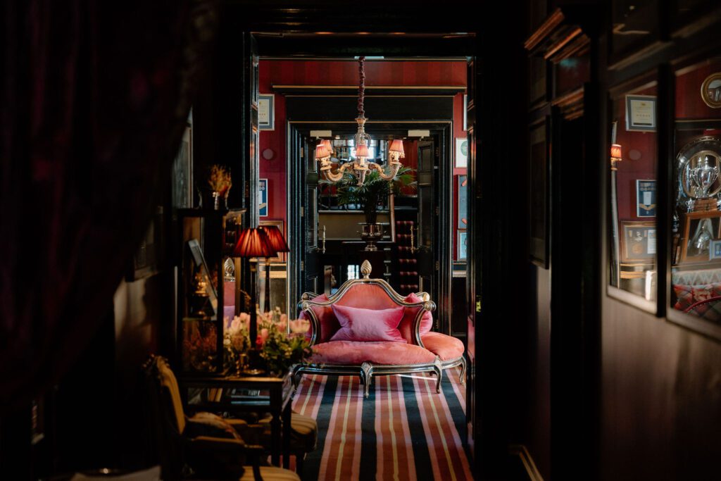 Pink chaise longue in a hallway with chandelier and dark red walls