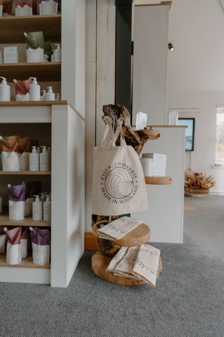 Essence of Harris tote bag hangs beside shelves of bottled products in the shop