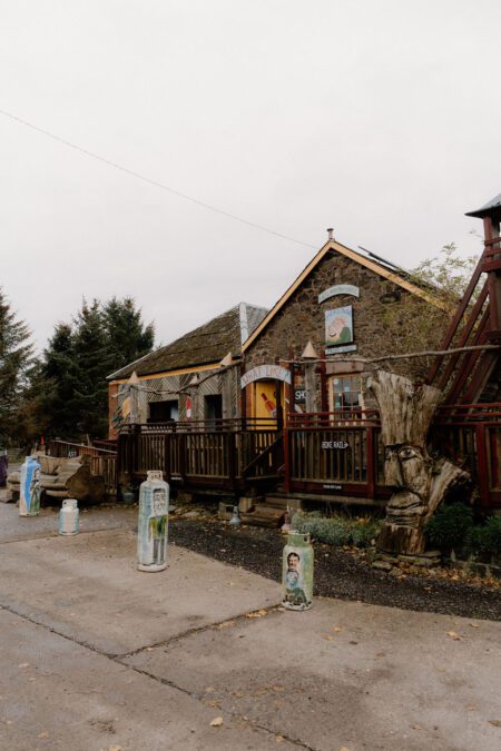 Painted milk churns line the path to a rustic stone shop with wooden decking