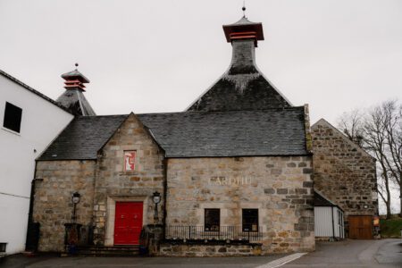 Cardhu distillery building with pagoda roofs and red door under grey sky