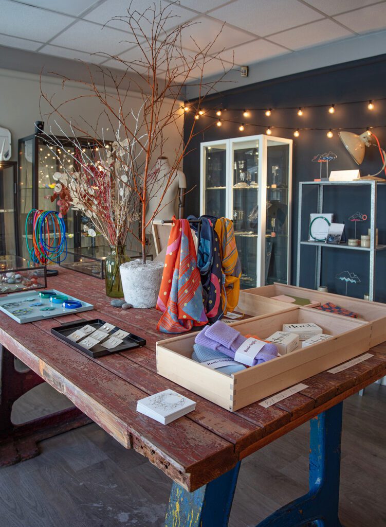 Coloured scarves, jewellery and wooden trays displayed on a rustic wooden table in a gift shop