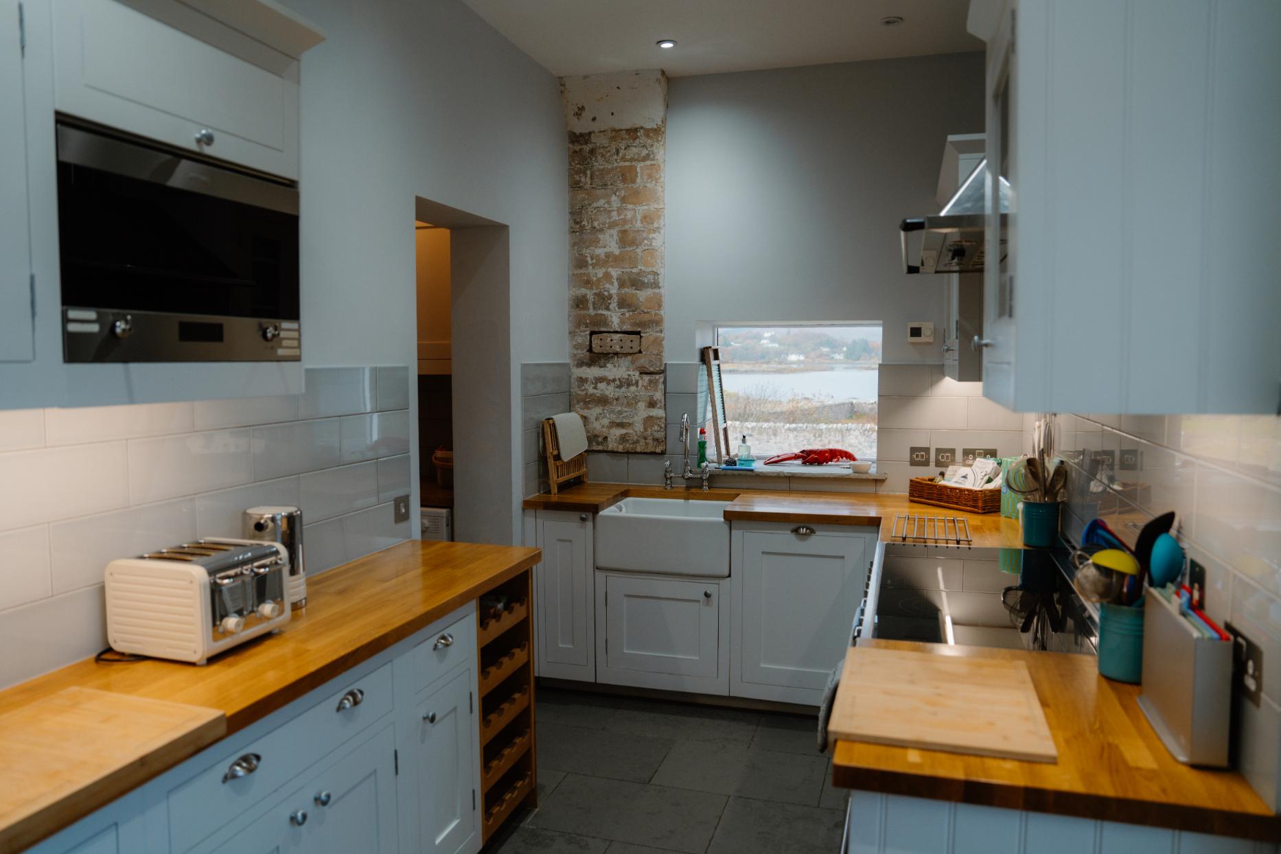 Narrow kitchen with wooden worktops, exposed stone wall and belfast sink