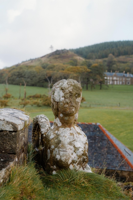 Lichen-covered stone sphinx statue overlooking a manor house and hillside