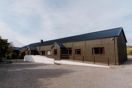 Long timber-clad building with a dark metal roof and red-framed windows