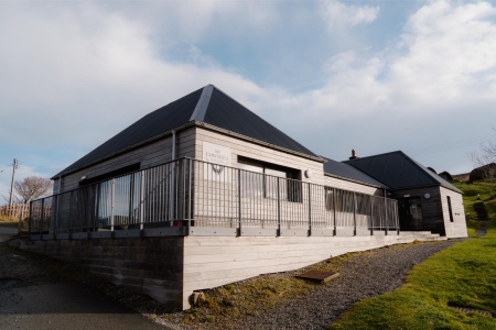 Timber-clad building with black roof and metal railings along a gravel path