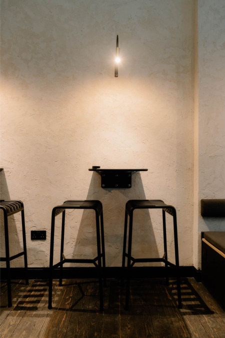 Black metal stools beneath a small wall lamp on textured plaster