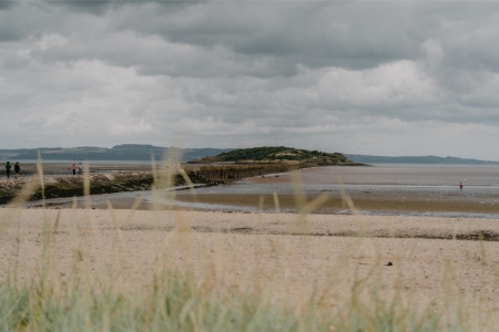 Marram grass frames a wide sandy beach with distant walkers and a wooden groyne