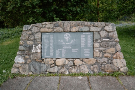 Stone memorial cairn with three engraved plaques listing names, set on grass