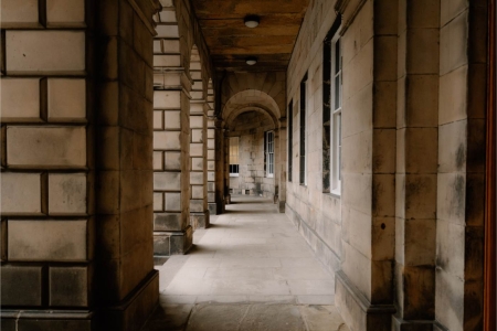 Stone colonnade with arched ceiling and windows along a covered walkway