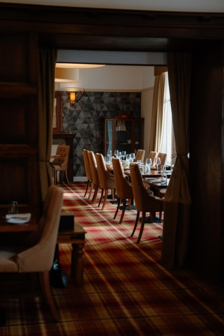 Dining room with tartan carpet, wine glasses set on long wooden tables
