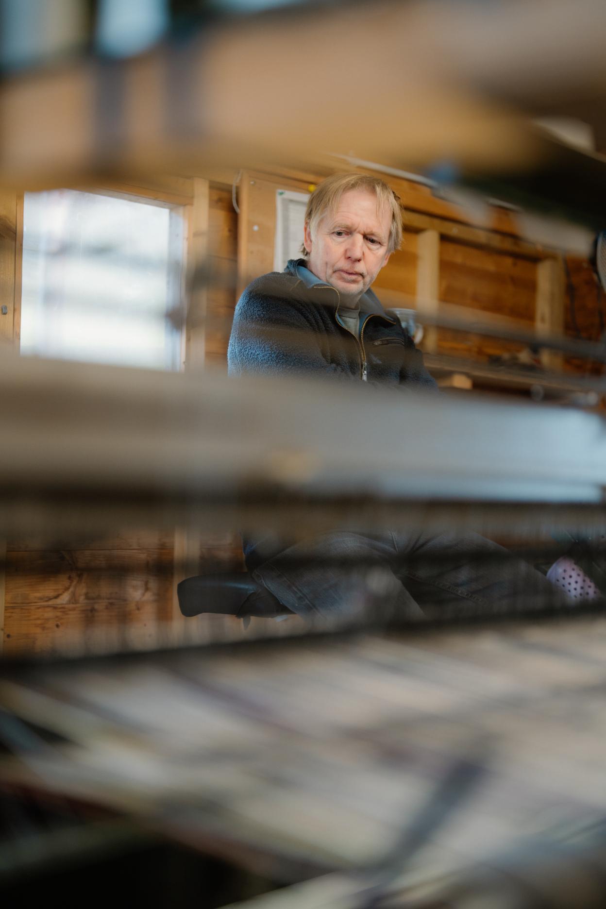 Weaver seated behind loom threads in a wood-panelled workshop