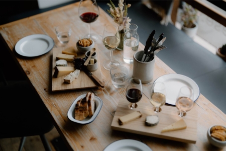 Wooden table set with cheese boards, wine glasses and bread on white plates