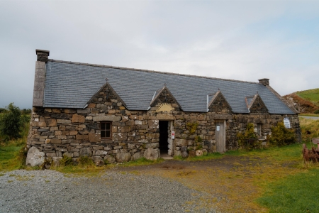 Long stone cottage with slate roof and three gabled dormers, doors open