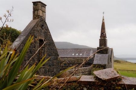 Stone chimney gable and church spire behind a moss-covered wall