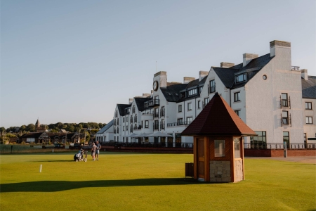 Golfers walk the fairway past a wooden shelter beside Carnoustie's hotel